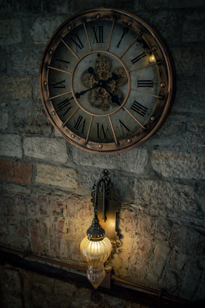 services-01 Vintage wall clock with Roman numerals and a glowing antique lamp on stone wall.
