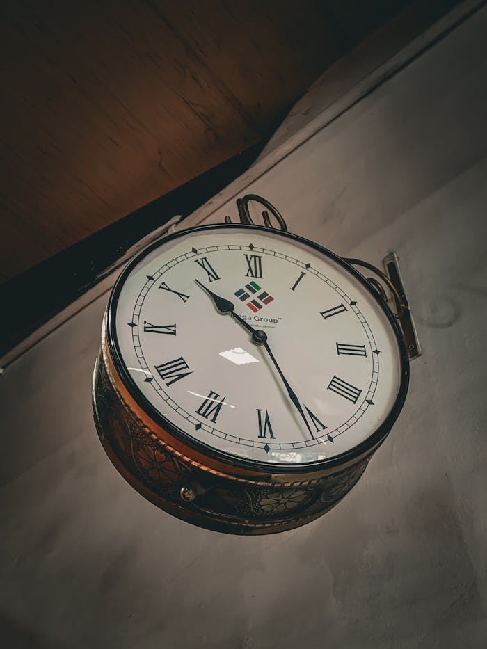 A vintage wall-mounted clock featuring Roman numerals and classic design, suitable for interiors.